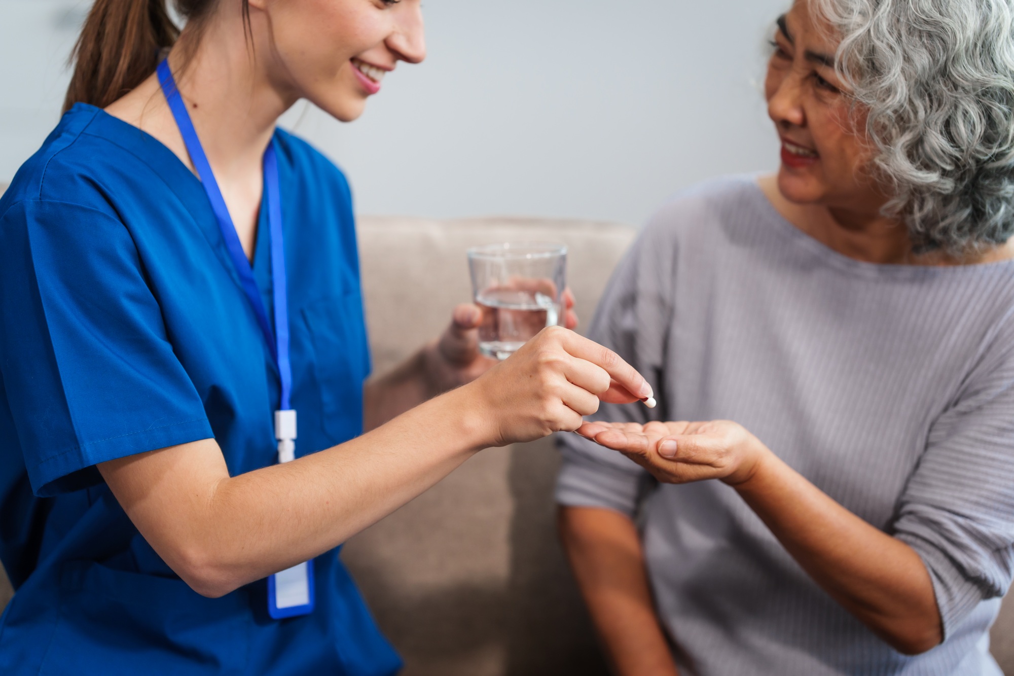 Caucasian female doctor provides a glass of water and medication pills to an elderly Asian